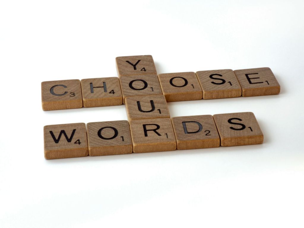 Scrabble tiles showing the words "Choose your words" arranged on a white plain background.
